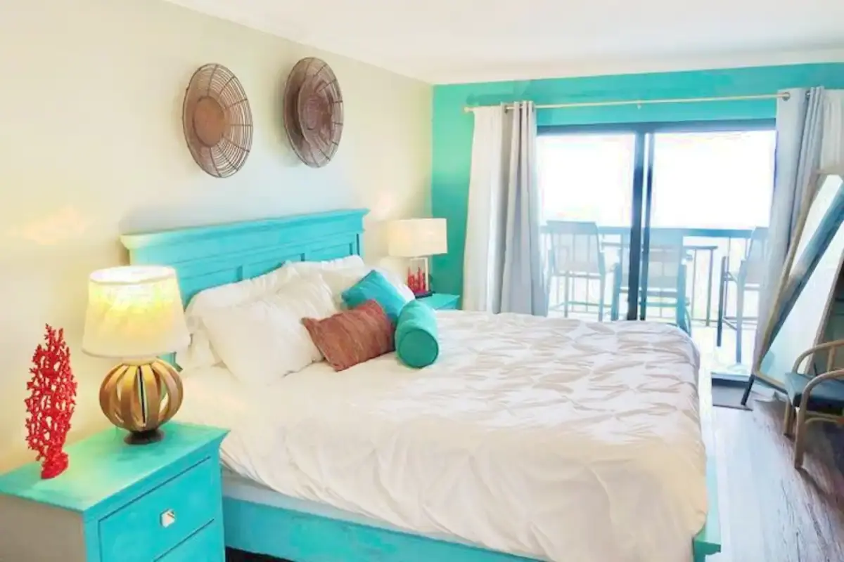 Turquoise-accented bedroom opening onto an ocean-view balcony